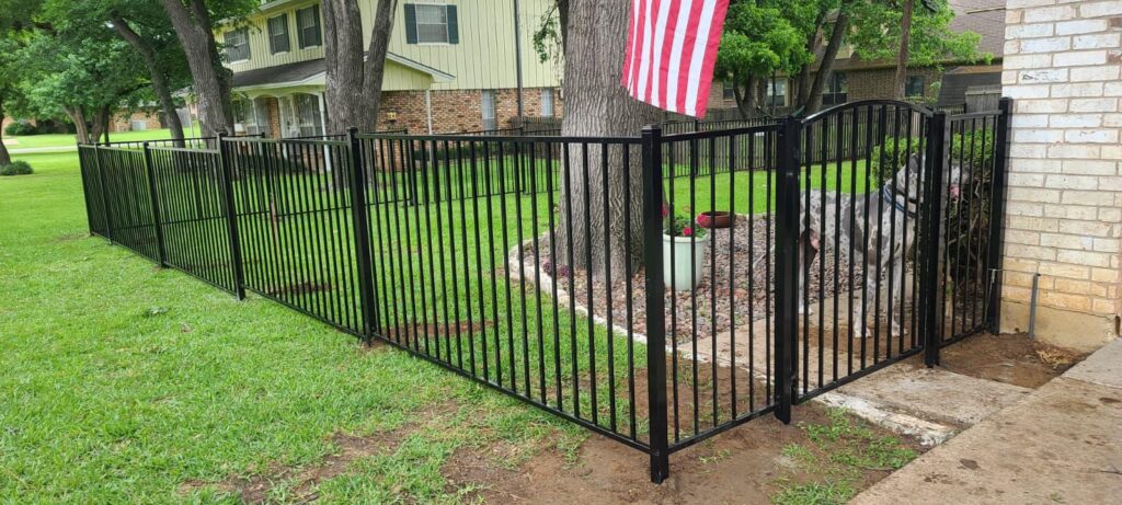 Black aluminum fence with an arched ornamental iron entry gate in a front yard