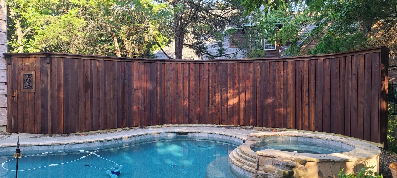 Curved dark-stained cedar privacy fence wrapping a backyard pool