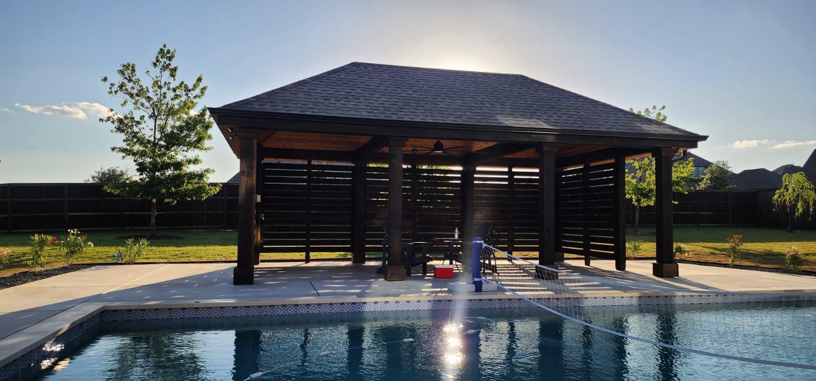 Dark-stained pavilion with a shingled hip roof built on a pool deck