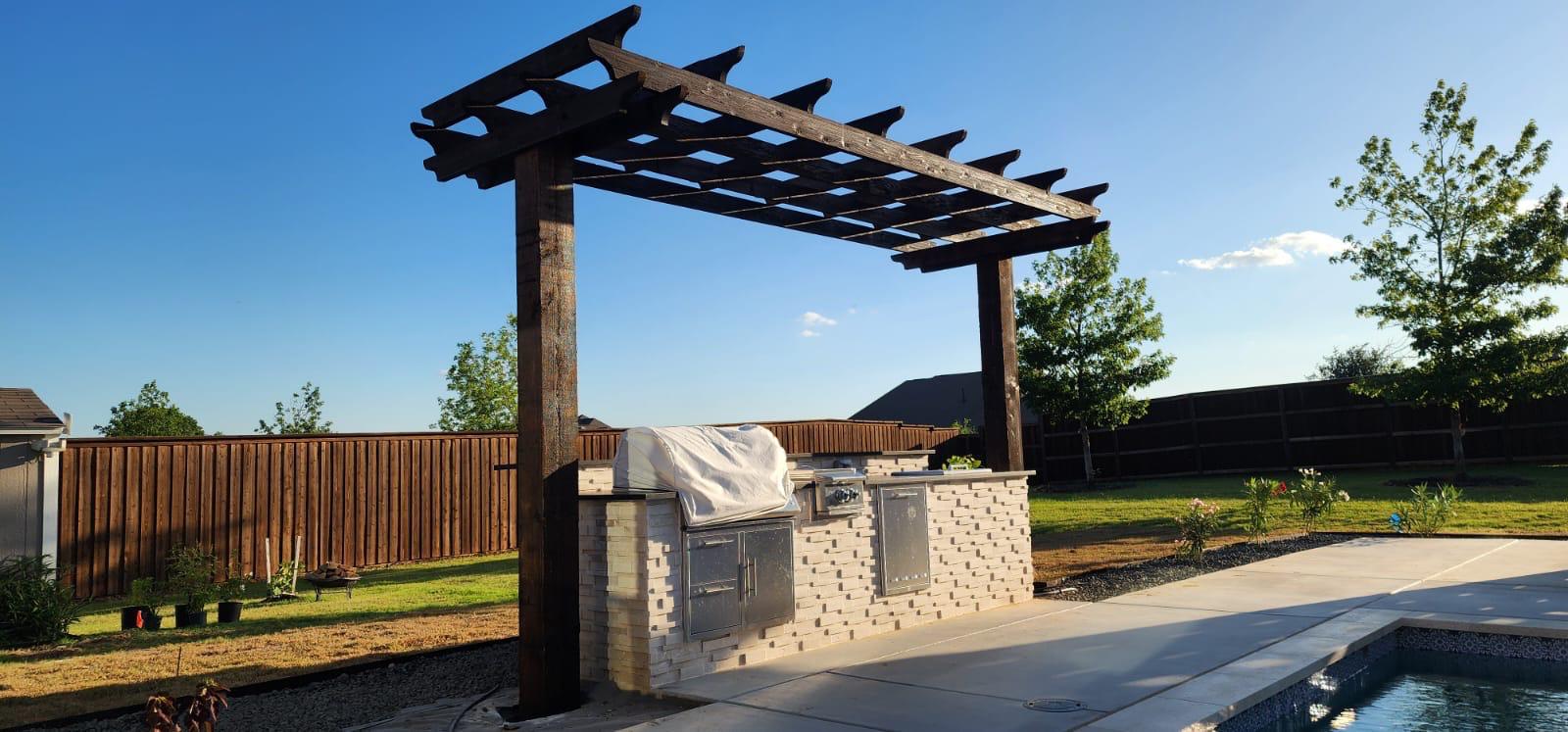 Wood pergola over a poolside outdoor kitchen with a built-in grill island