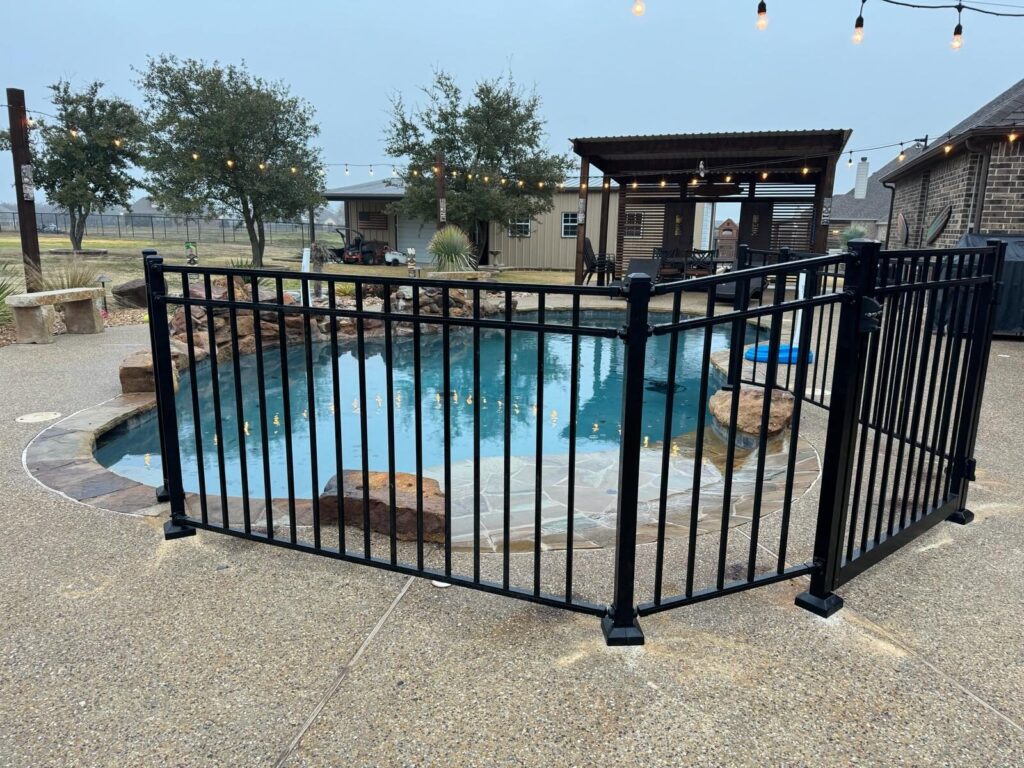 Black metal pool fence panels enclosing a freeform pool with a stone waterfall