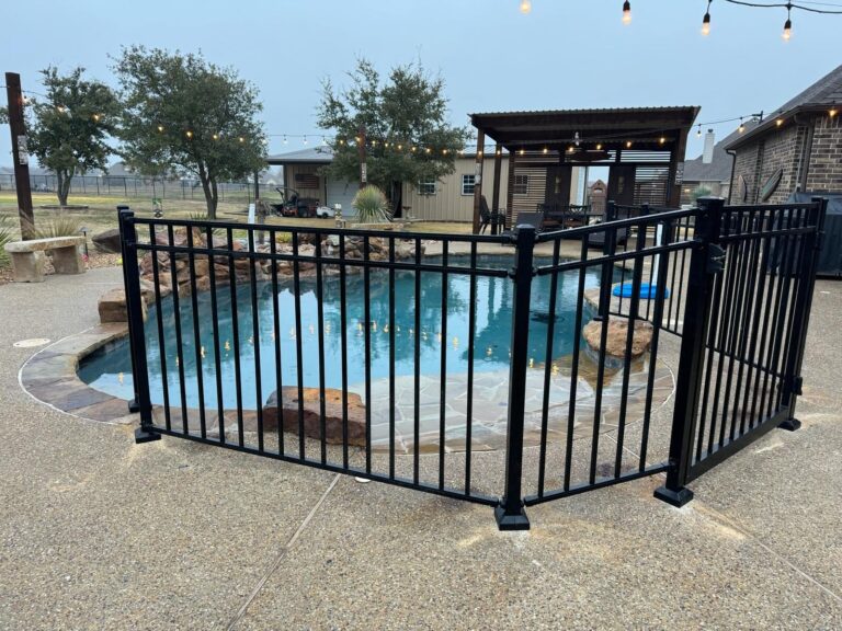 Black metal pool fence panels enclosing a freeform pool with a stone waterfall