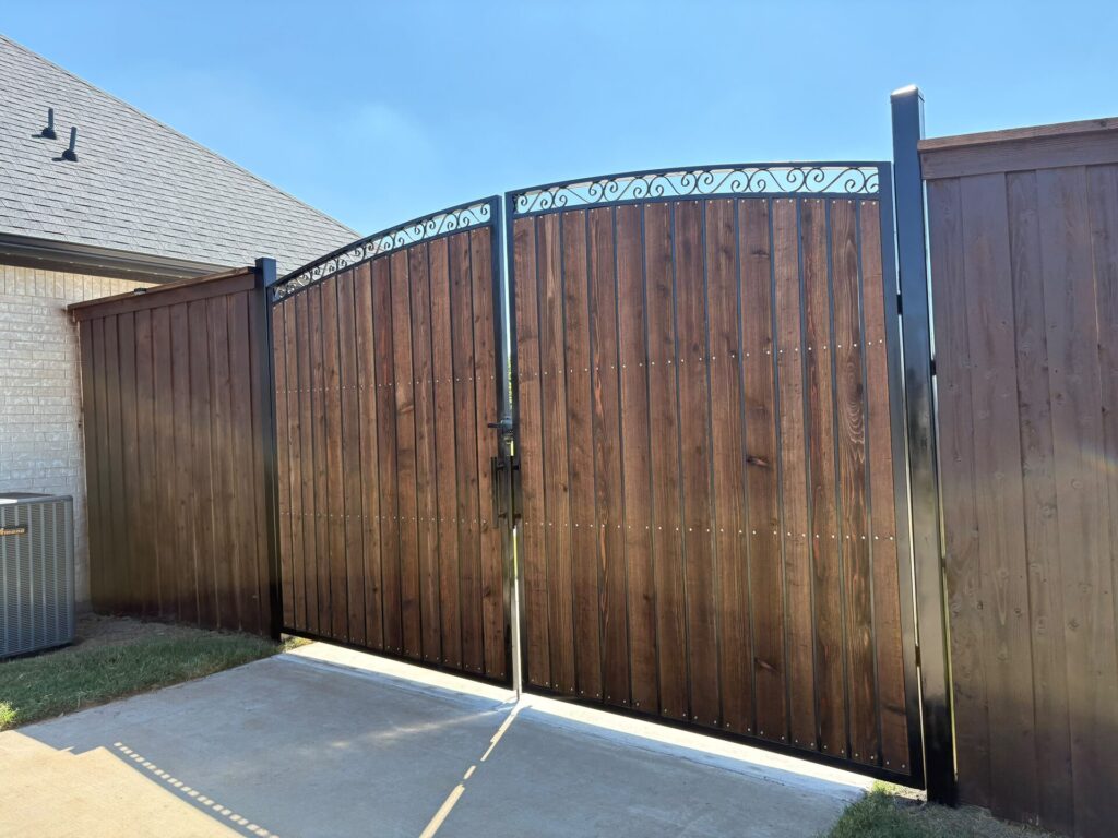 Cedar double driveway gate with iron arch set between stained cedar privacy fence sections