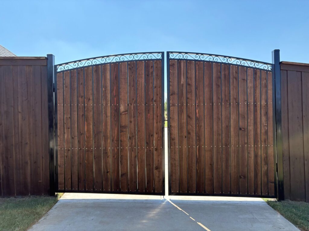 Stained cedar double driveway gate with black steel frame and decorative iron scroll arch