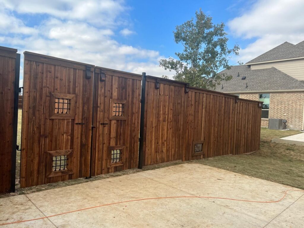 Stained cedar double driveway gates with iron grille windows, angled view