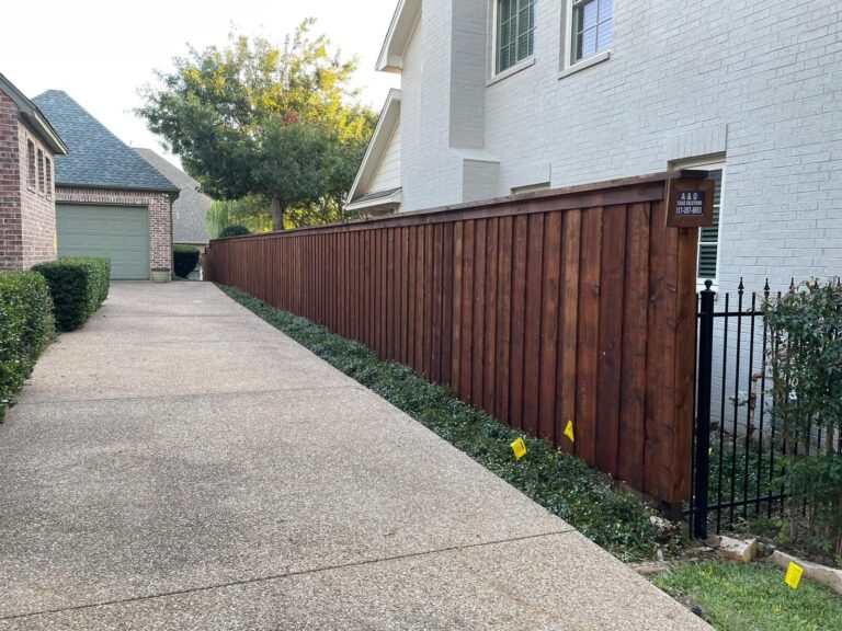 Stained cedar privacy fence along a driveway meeting a black iron fence