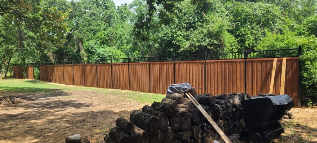 Stained cedar fence with a black iron topper along a wooded lot