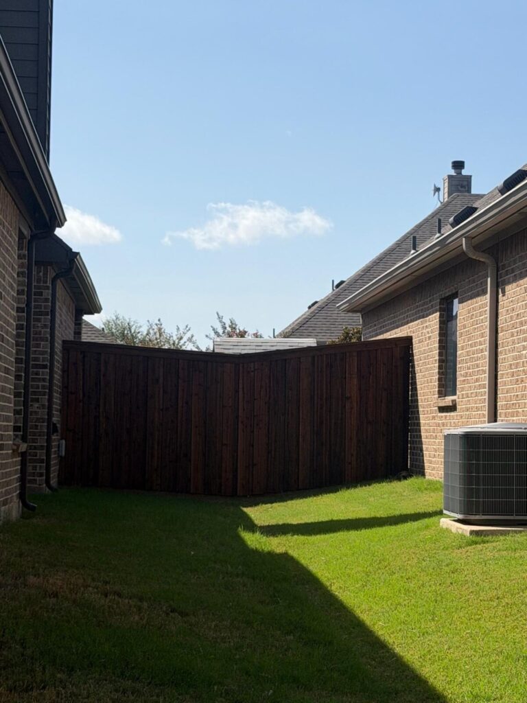 Stained cedar privacy fence enclosing a backyard between two brick homes