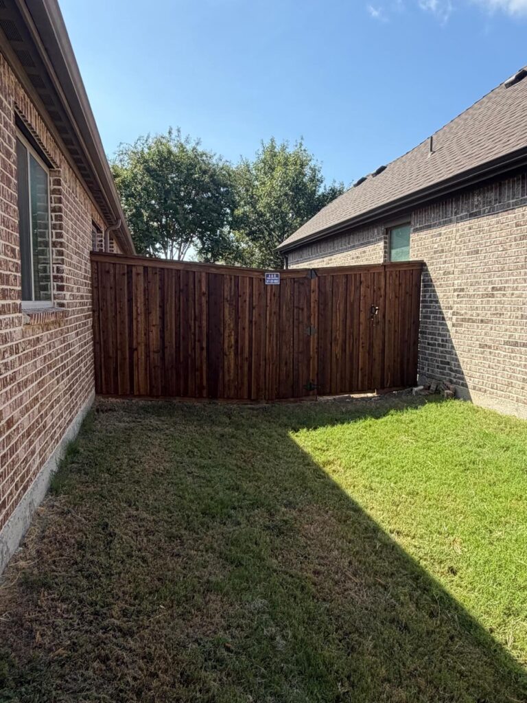 Stained cedar privacy fence closing off a narrow backyard beside a brick house