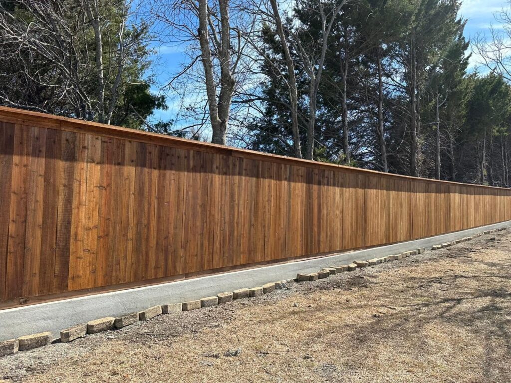Cedar privacy fence built on a concrete mow strip along a treeline