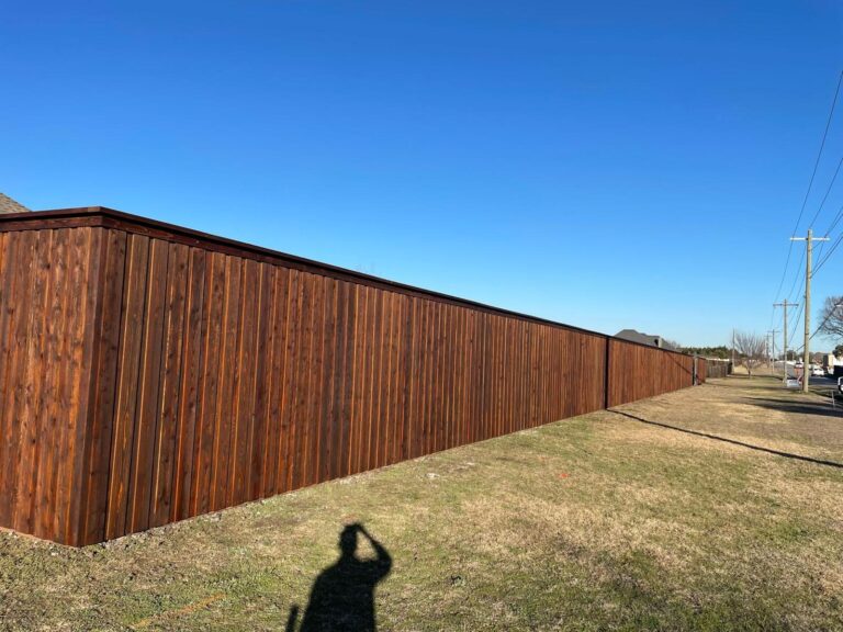 Long stained cedar privacy fence along an open field under blue sky