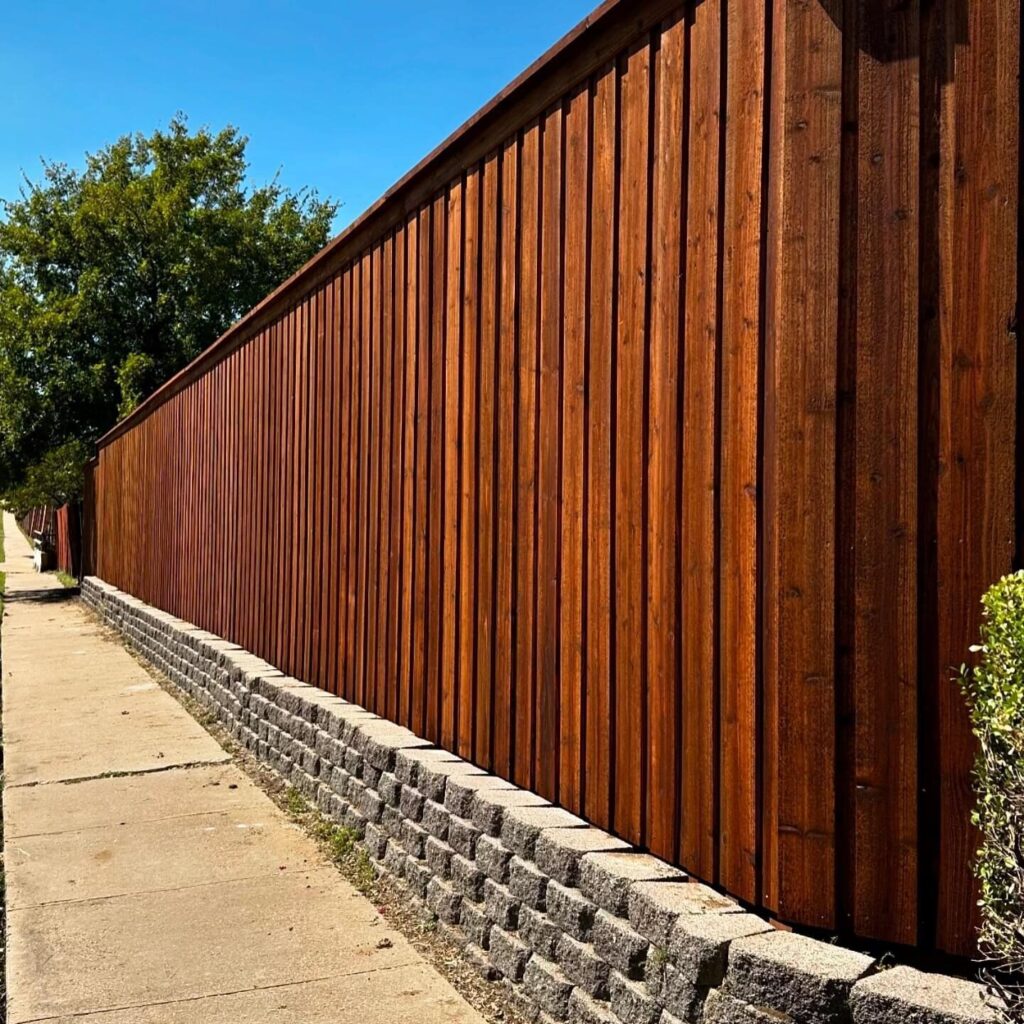 Tall stained cedar fence on a block retaining wall beside a sidewalk