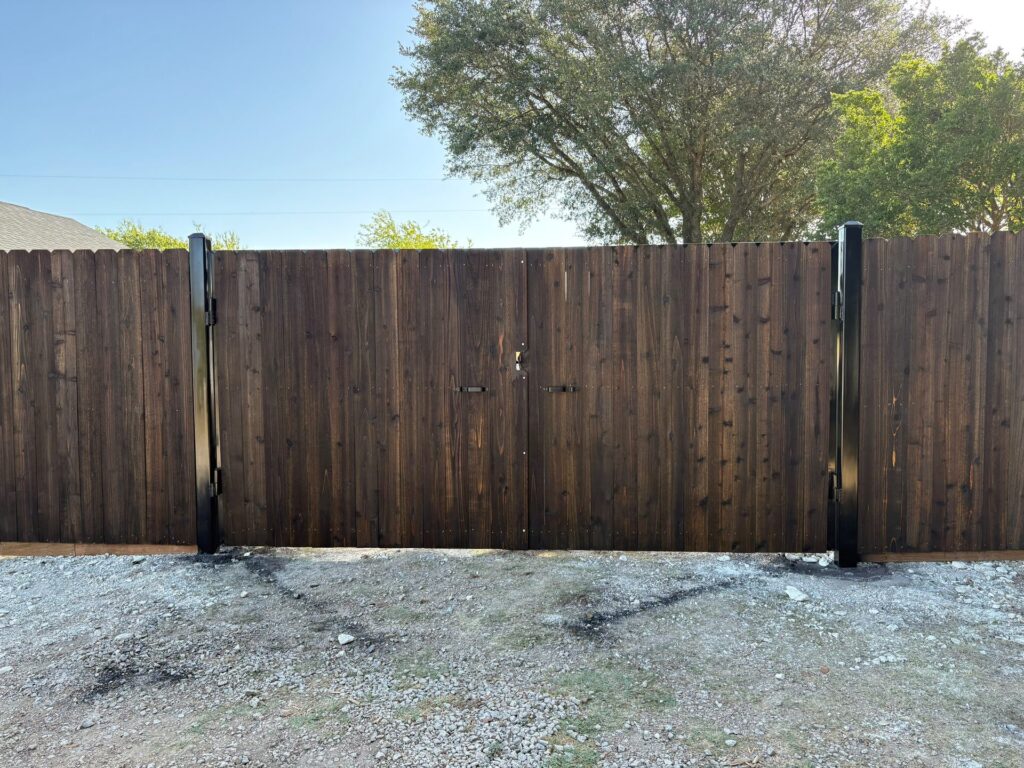 Dark-stained wood privacy fence with a flush double gate hung on black steel posts
