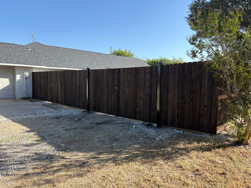Long run of dark-stained wood privacy fence on black steel posts beside a gravel drive