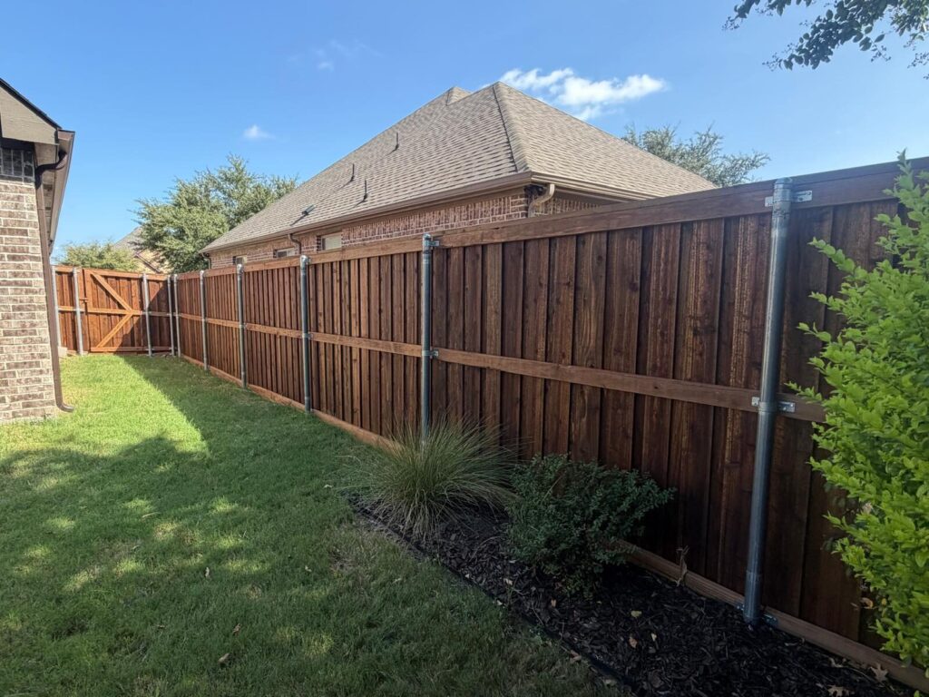 Stained cedar privacy fence on galvanized steel posts along a landscaped backyard