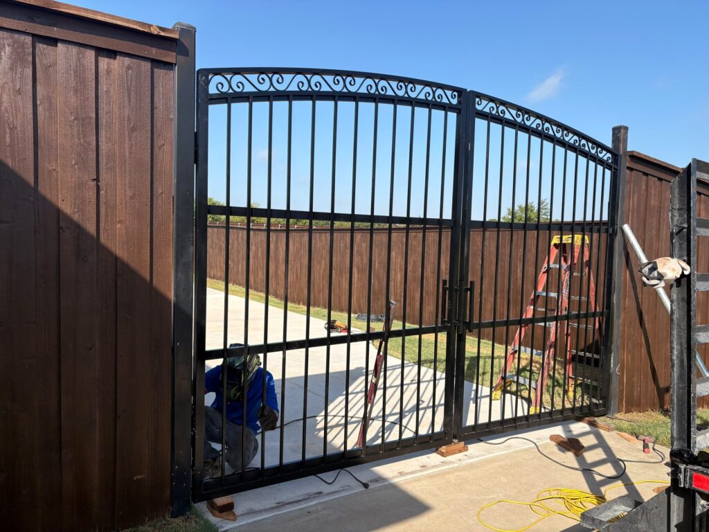 Black wrought iron arched double gate being installed between cedar fence sections